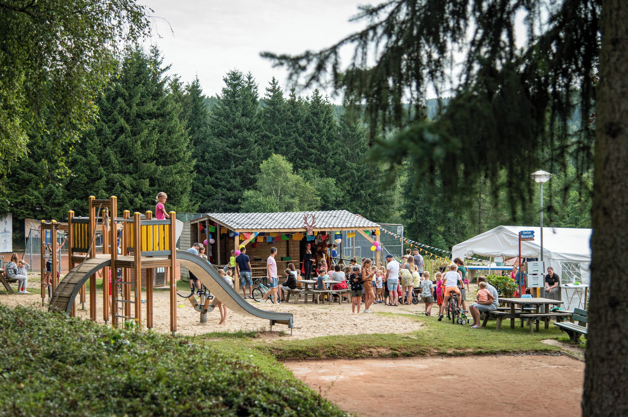 A playground with slides and climbing structures, surrounded by trees and a picnic area with tables and benches.