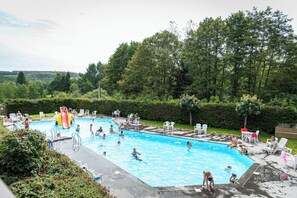 Ein Schwimmbecken mit Rutsche, umgeben von Grünflächen und Terrassenmöbeln.