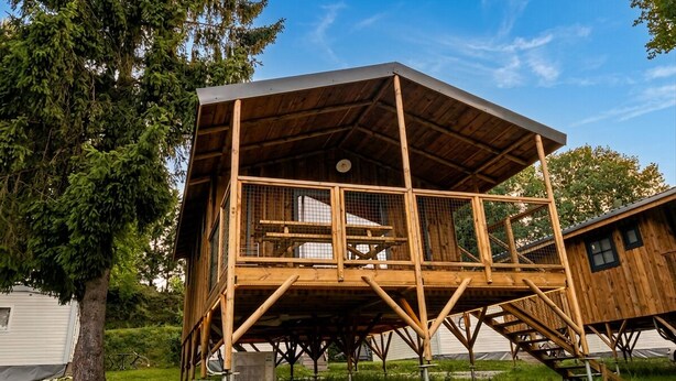 Una cabaña de madera con balcón, escalera y un nivel superior cubierto.