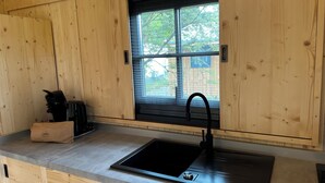 Una cocina con armarios de madera, un lavamanos negro y una ventana con vistas a árboles.