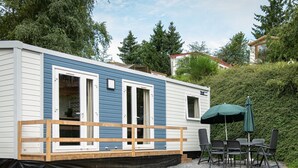 A mobile home with a deck, outdoor seating, and a covered patio area. - The Grande Large mobile home is a fully equipped, comfortable accommodation for 6 people, ideal in any season thanks to its three bedrooms, terrace, air conditioning, and central heating. (Dochamps)