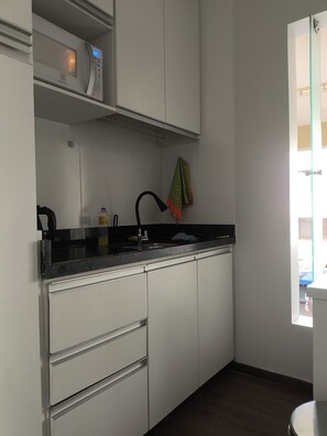 Una cucina con mobili bianchi, un forno a microonde, un lavandino e una finestra con vista.