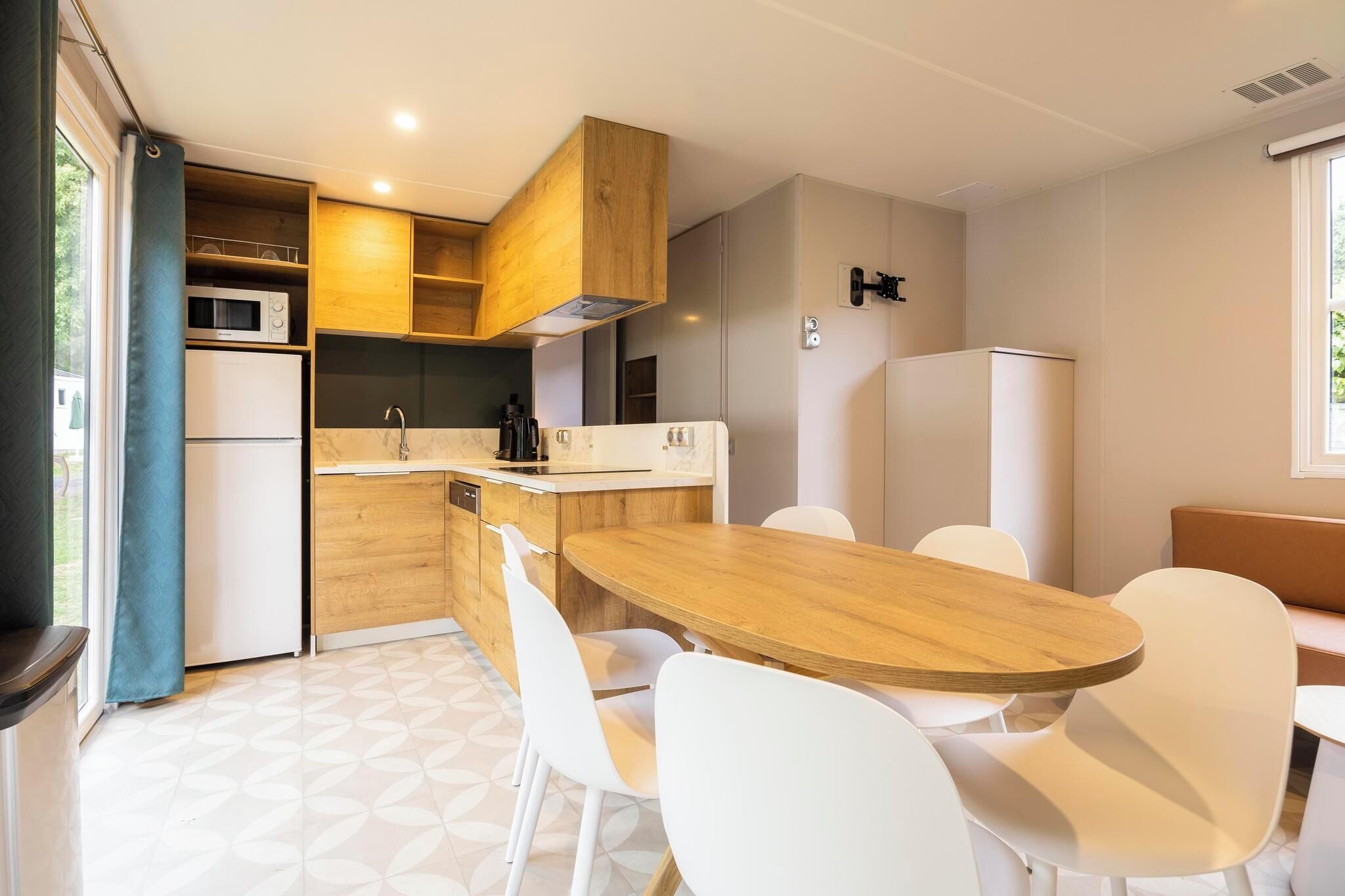 Een compacte keuken met houten kastjes, een magnetron, een gootsteen en een eethoek met een houten tafel en witte stoelen.