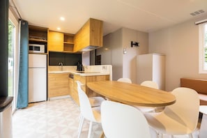 Cocina compacta con gabinetes de madera, microondas, lavamanos y comedor con mesa de madera y sillas blancas.