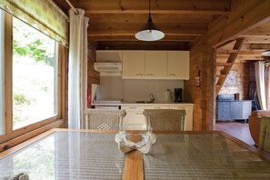 A wooden cabin interior with a dining table, kitchen area, and a view of greenery outside. - This charming two-story wooden Finnish chalet accommodates up to 5 people in two bedrooms for a cozy retreat in the heart of the Ardennes. (Dochamps)