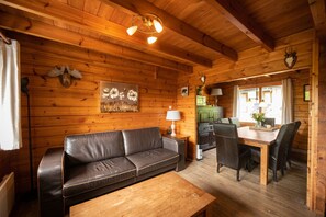 A cozy cabin interior with a wooden ceiling, a sofa, a dining table with chairs, and a fireplace. - This charming two-story wooden Finnish chalet accommodates up to 5 people in two bedrooms for a cozy retreat in the heart of the Ardennes. (Dochamps)