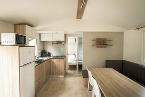 Cozinha compacta com micro-ondas, fogão e armários, que dá acesso a um quarto com cama e janela.