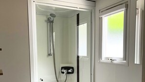Um chuveiro com divisória de vidro, chuveiro manual e painel de controle na parede.