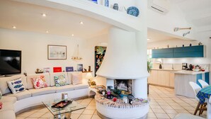 Uma sala de estar moderna com lareira, um sofá, uma mesa de centro e uma cozinha ao fundo.
