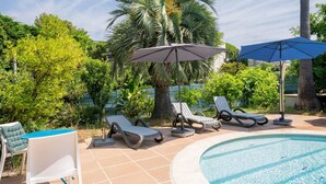 Uma área à beira da piscina com espreguiçadeiras, piscina e guarda-sóis.