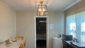 A compact kitchen with a dining table, chairs, a refrigerator, a microwave, and a window with curtains. - Comfortable 1-bedroom apartment close to Beach with AC- Vero Beach (Vero Beach)