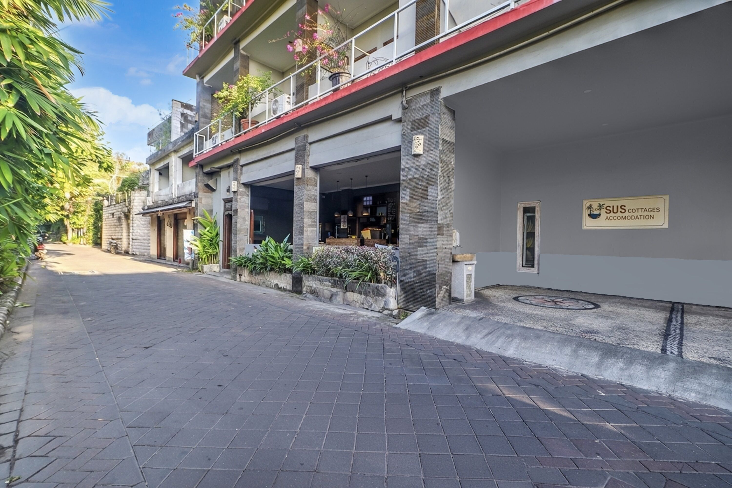A building with a sign for SUS Cottages Accommodation, a paved walkway, and a stone facade.