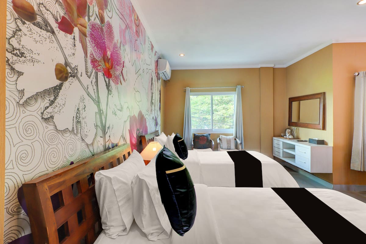 A hotel room with two beds, a desk, a window, and a wall with a floral mural.