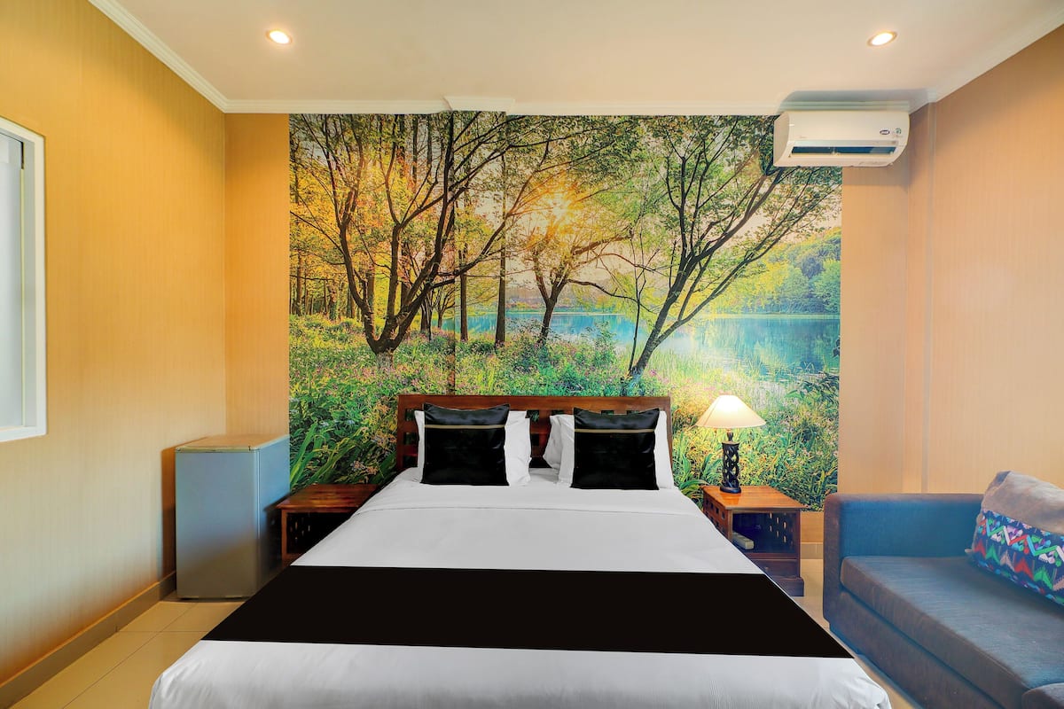 A hotel room with a bed, a small table with a lamp, a sofa, and a wall-mounted air conditioner.