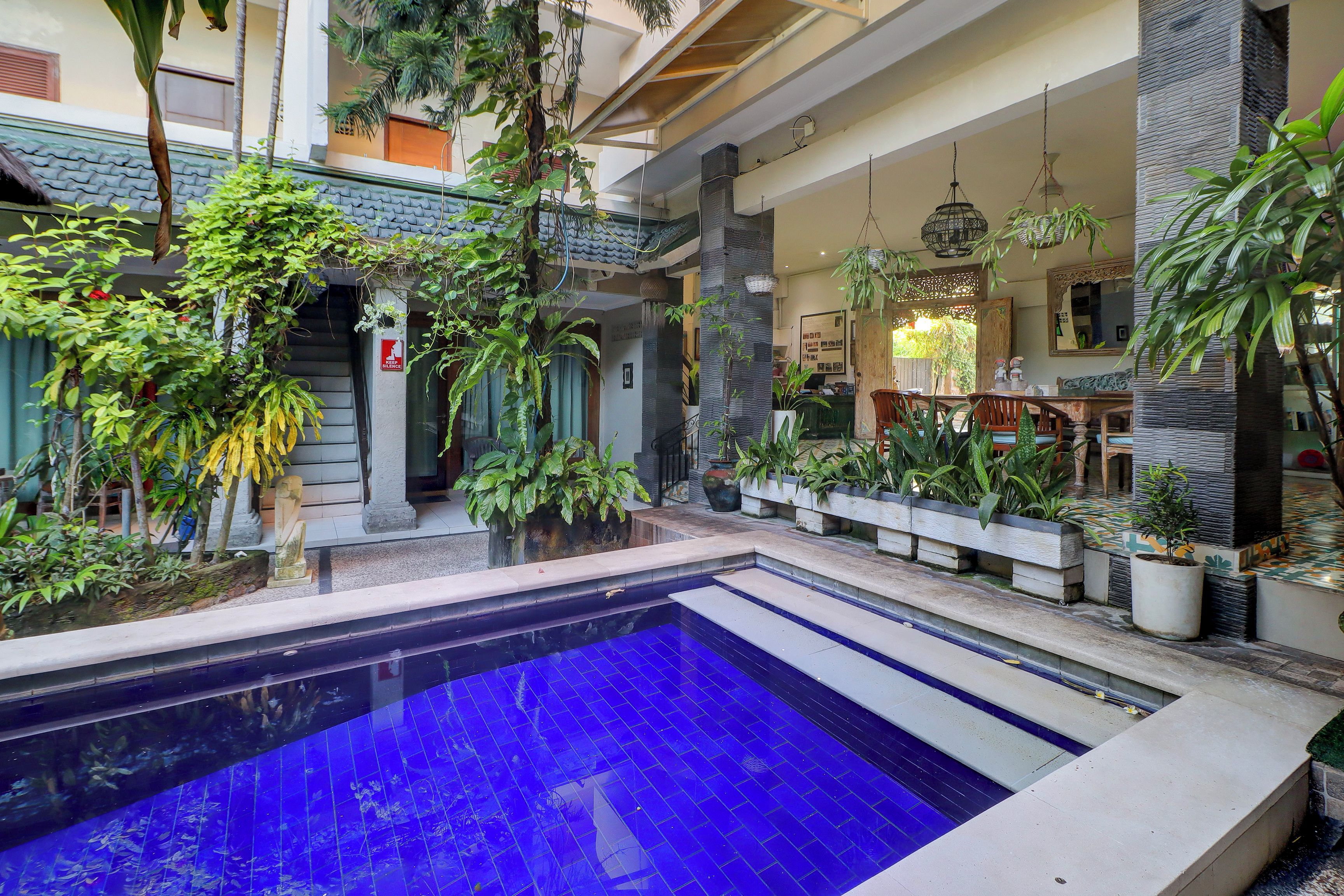 A pool area with a blue-tiled pool, surrounded by potted plants and a staircase leading to upper levels.