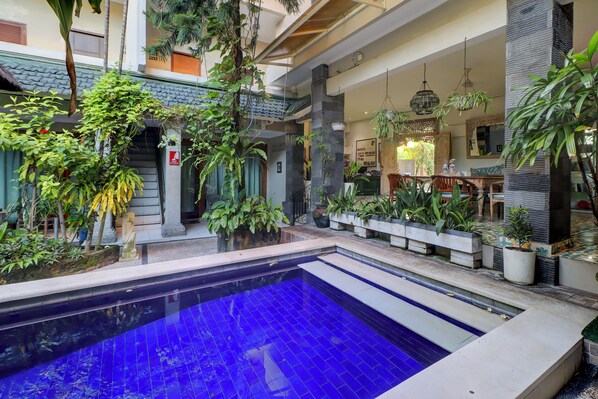 Zona de piscina con piscina de azulejos azules, rodeada de plantas en macetas y una escalera que lleva a niveles superiores.
