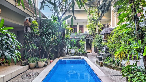 A swimming pool surrounded by lush greenery, with a building in the background. - Townhouse Oak Su's Cottage Near Legian Beach (Kuta)