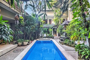 A swimming pool surrounded by lush greenery, with a building in the background. - Townhouse Oak Su's Cottage Near Legian Beach (Kuta)