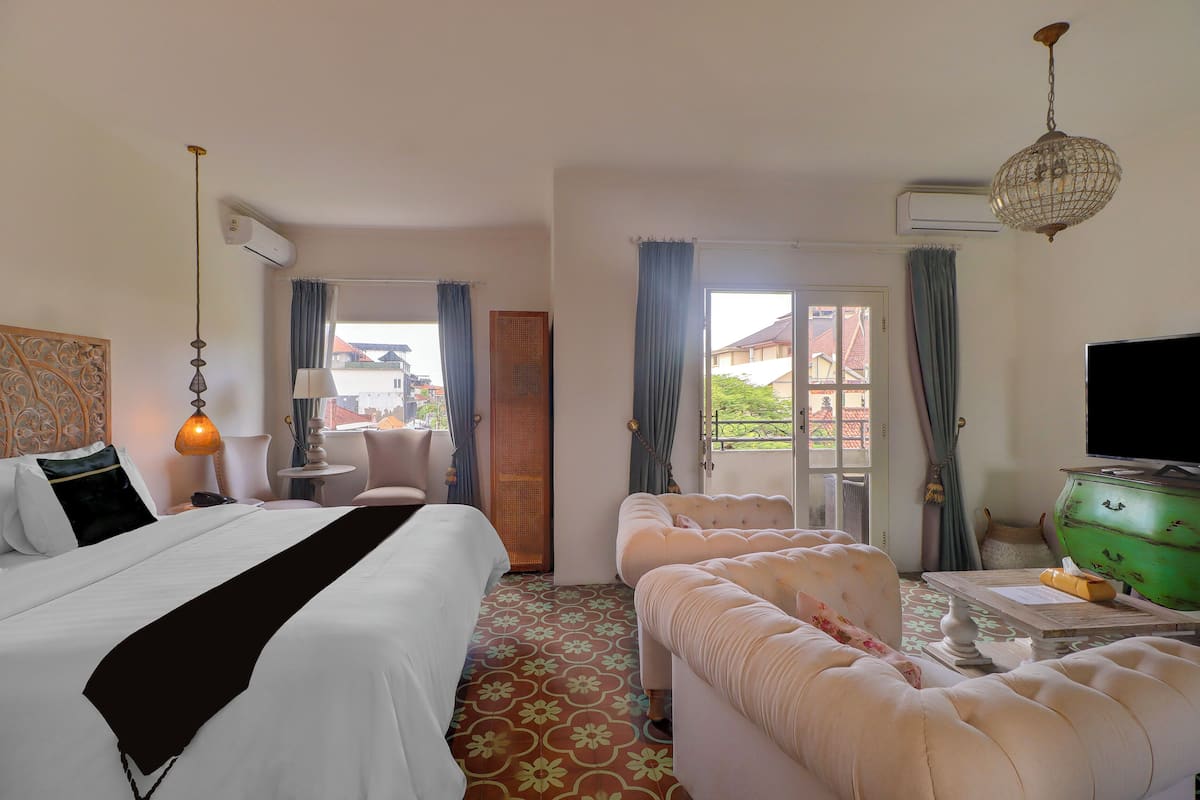 A hotel room with a bed, a sofa, a television, and a window with curtains.