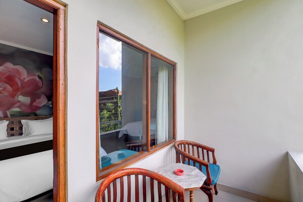 A balcony with a wooden chair, a small table, and a large window. - Townhouse Oak Su's Cottage Near Legian Beach (Kuta)
