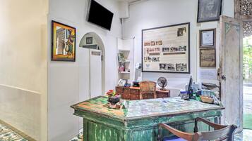 Una habitación con un escritorio verde, una silla, un televisor montado en la pared y un tablón de anuncios con diversas imágenes y texto.