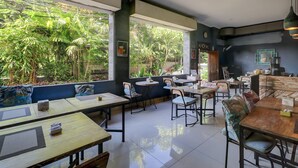 A restaurant with tables and chairs, large windows, and a view of greenery outside. - Townhouse Oak Su's Cottage Near Legian Beach (Kuta)