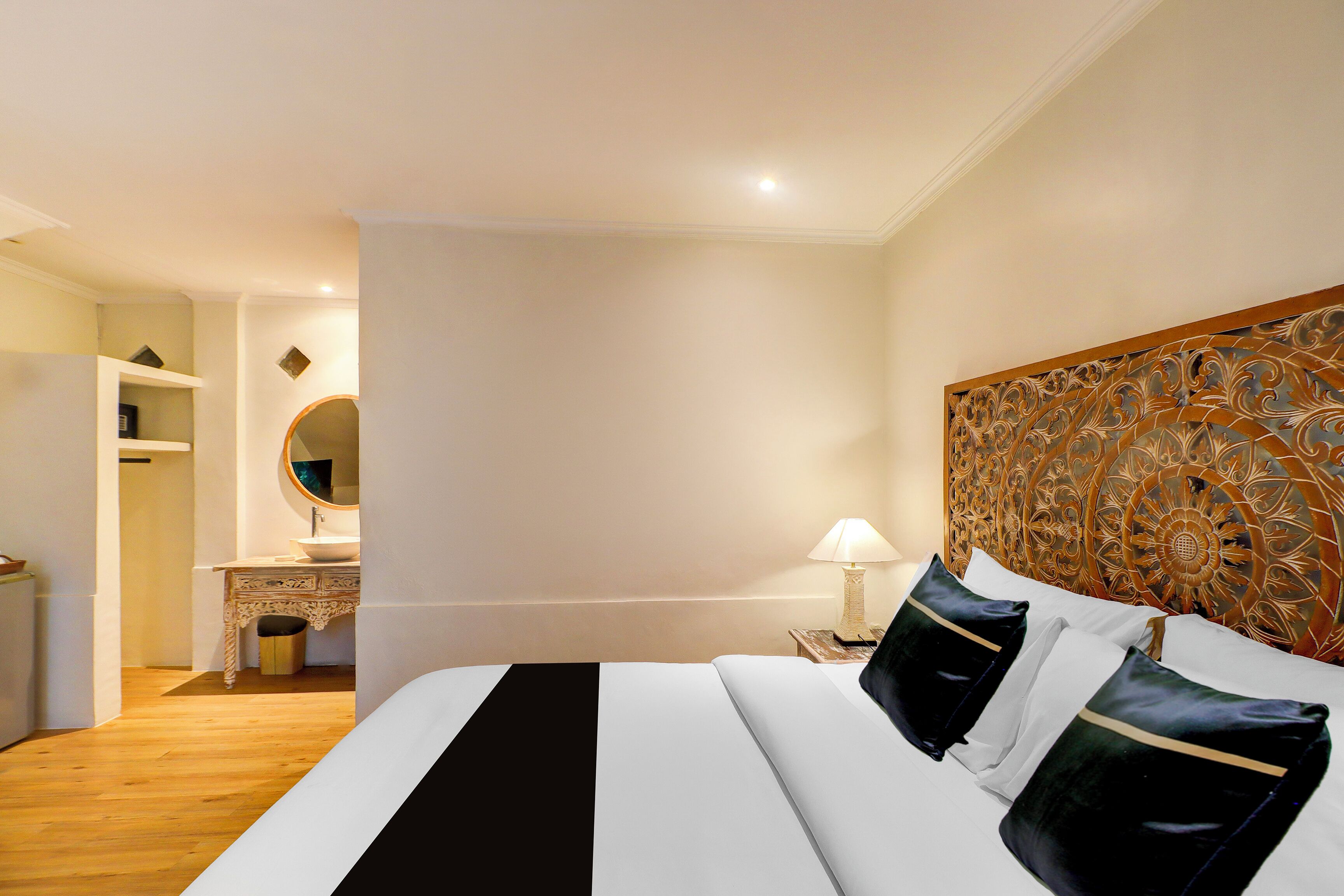Quarto de hotel com uma cama, mesa de cabeceira, abajur, cômoda, espelho e cabeceira decorativa.