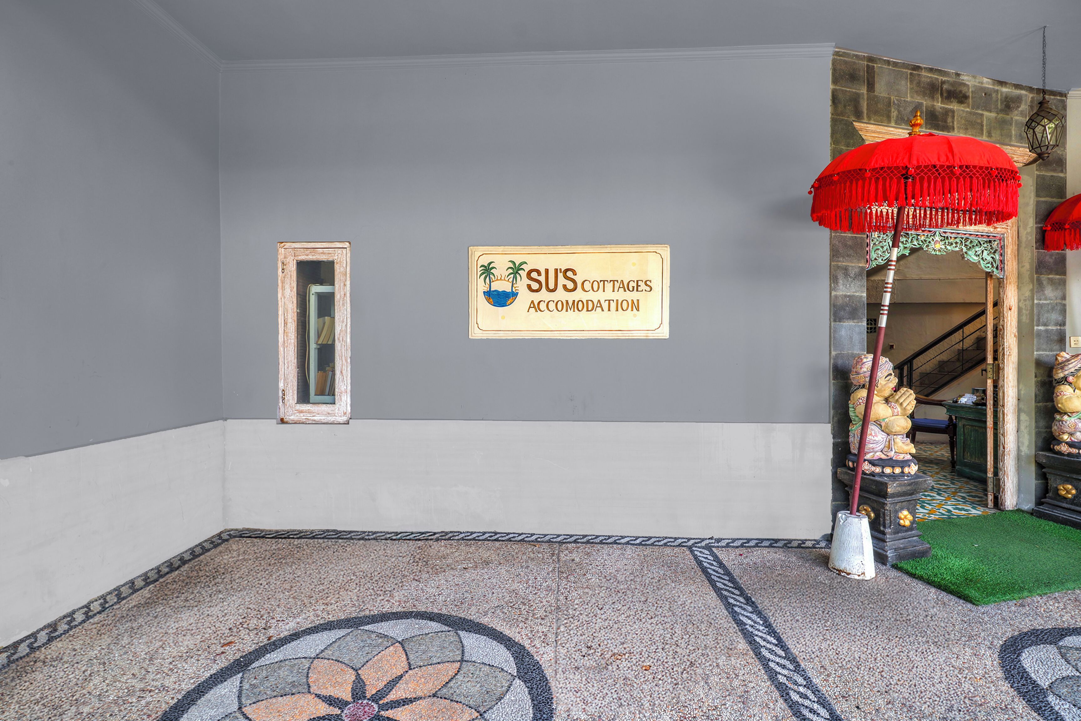 A room with a tiled floor, a sign for 'SUS Cottages Accommodation,' a mirror, and a red umbrella.