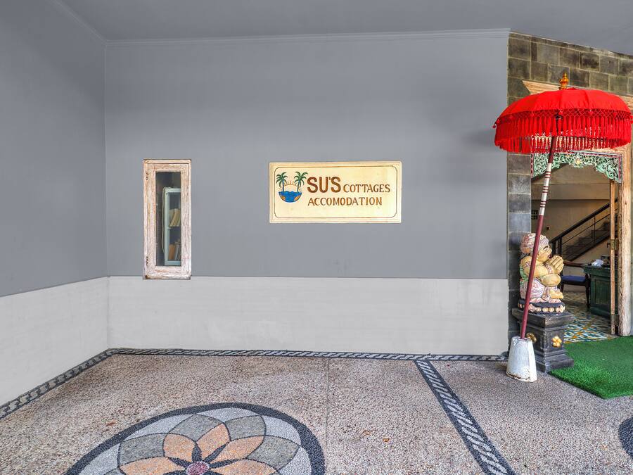 A room with a tiled floor, a sign for 'SUS Cottages Accommodation,' a mirror, and a red umbrella.