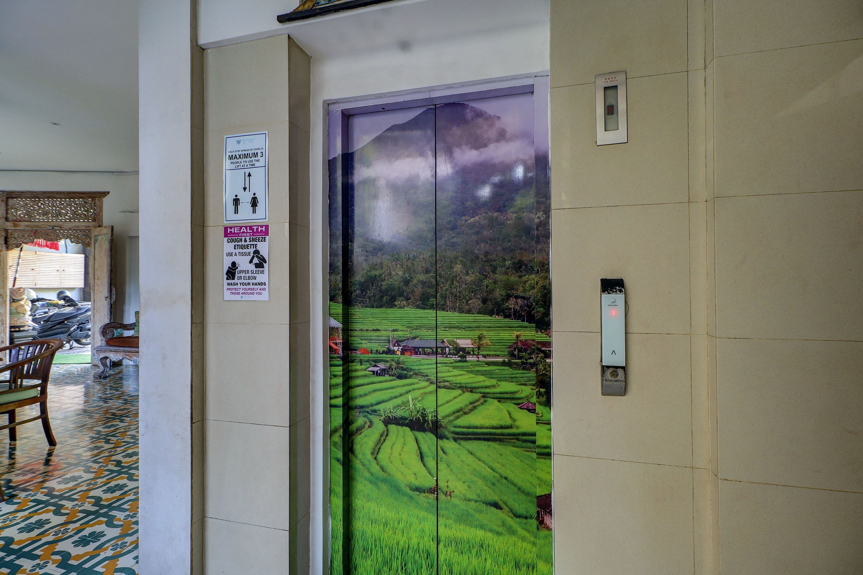 An elevator with a mural of a green landscape, a health poster, and a hand sanitizer dispenser.