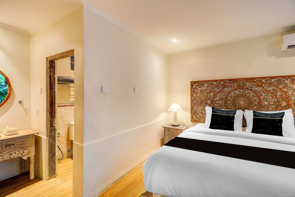 A hotel room with a bed, bedside table, lamp, and a mirror.