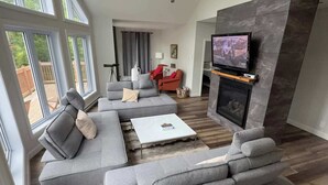 Ein modernes Wohnzimmer mit grauen Sofas, einem weißen Couchtisch, einem Kamin und einem an einer Steinwand befestigten Fernseher.