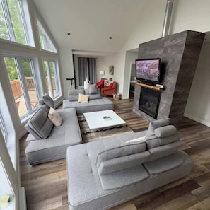A modern living room with grey sofas, a white coffee table, a fireplace, and a TV mounted on a stone wall. - Pool Table, Private Beach | Breakfast Included (Labelle)