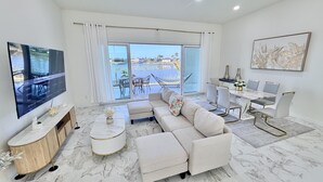 Una sala de estar moderna con un televisor grande, un sofá, un comedor y vistas al exterior.