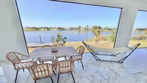 Un comedor con mesa y sillas, una hamaca y vistas a un lago y casas.