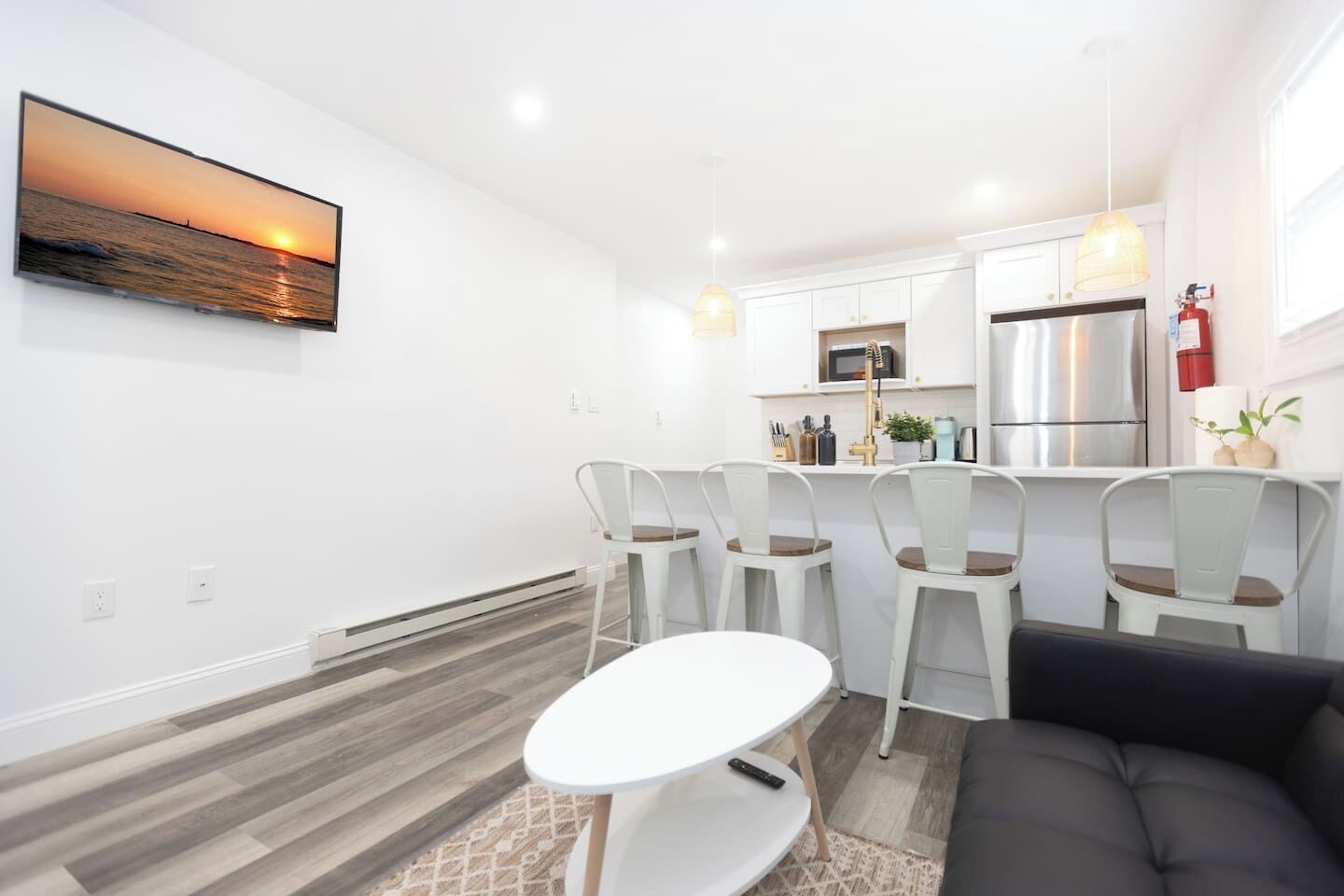 Una cocina moderna con armarios blancos, un refrigerador de acero inoxidable y un microondas. Hay un comedor con una mesa blanca y cuatro sillas.