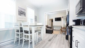 A modern kitchen with white cabinets, a dining table with chairs, a sofa, and a TV mounted on the wall. - Crest 2 Coastal Stay, 1st fl, AC, KB, Free Parking (Wildwood Crest)