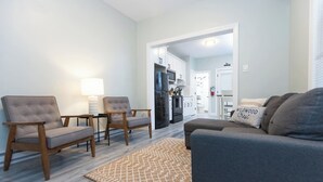 A living room with a grey sofa, two armchairs, a coffee table, and a patterned rug. A kitchen is visible in the background. - Crest 2 Coastal Stay, 1st fl, AC, KB, Free Parking (Wildwood Crest)