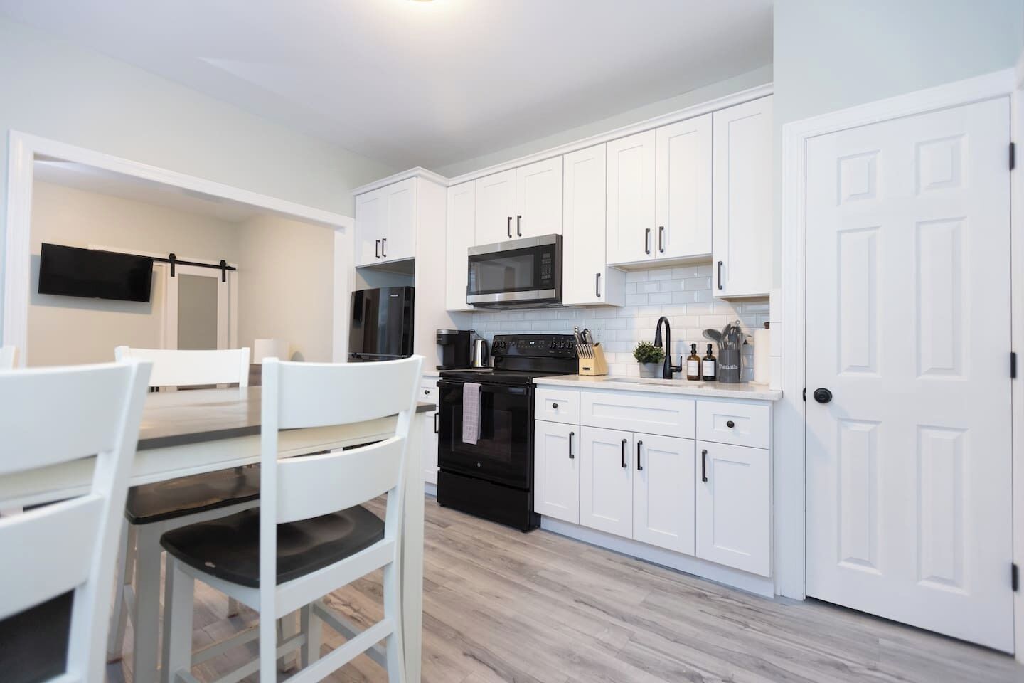 Une cuisine moderne avec des meubles blancs, un four noir, un micro-ondes et un coin repas avec des chaises blanches.