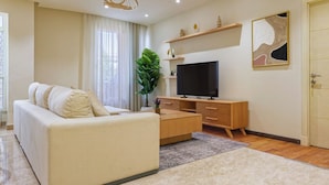 A modern living room with a sofa, TV, wooden cabinet, and a large plant. - VESTA  - Luxury APT - 4BR - New Cairo (II) (New Cairo City)