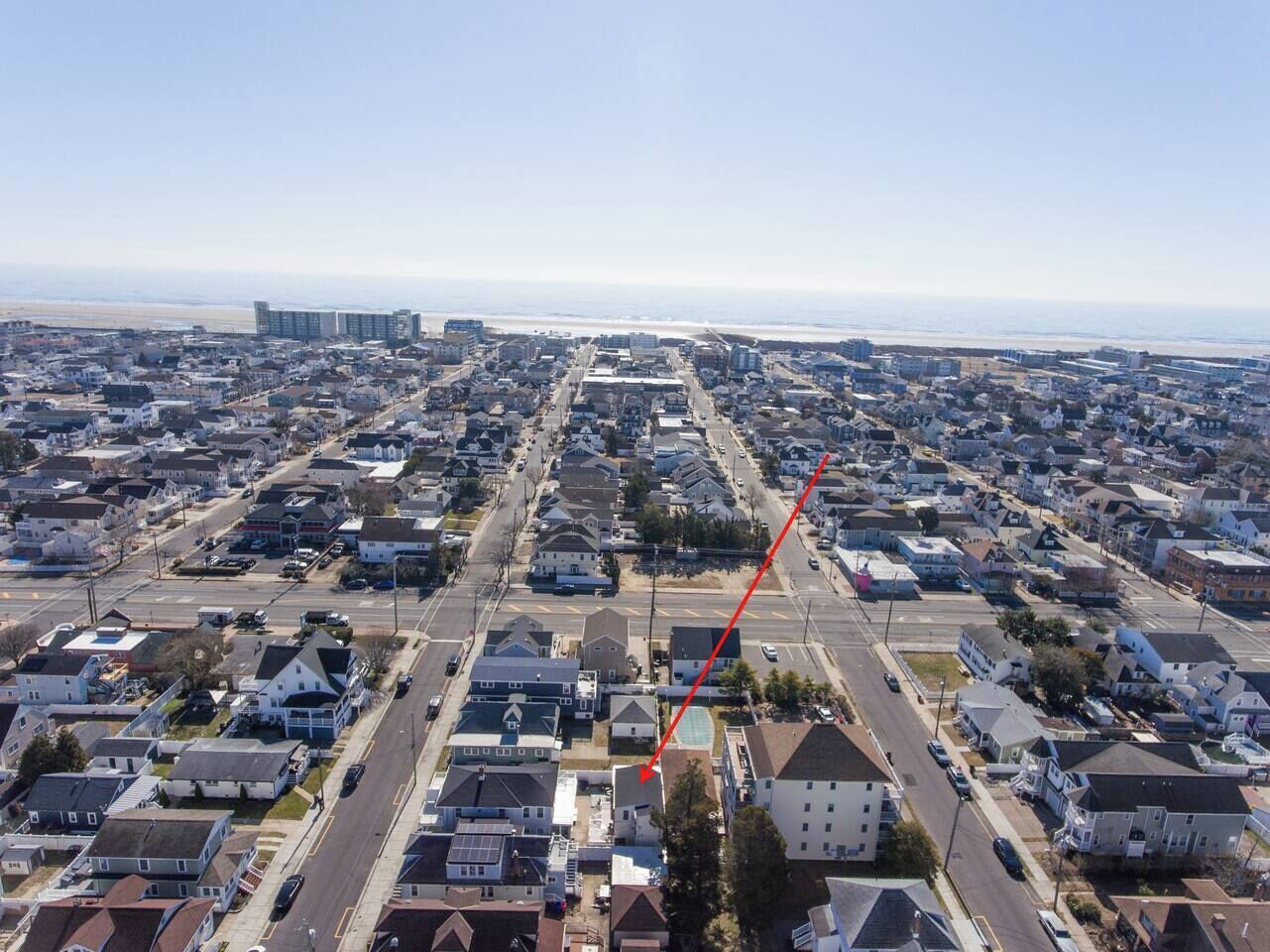 An aerial view of a residential area with houses, streets, and a beach in the background.