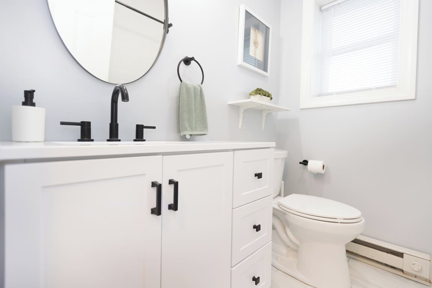 A modern bathroom with a white vanity, black faucet, and a toilet.