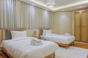 A hotel room with two beds, a large window with curtains, a wooden wardrobe, and a white rug. - VESTA  - Luxury APT - 4BR - New Cairo (III) (New Cairo City)