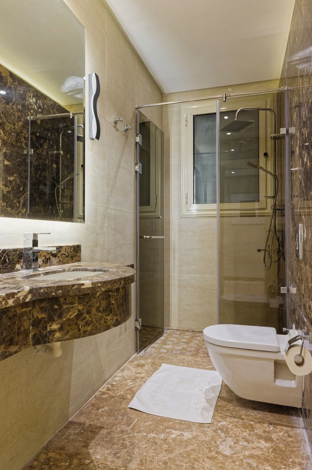 A modern bathroom with a marble vanity, a glass shower enclosure, and a toilet.