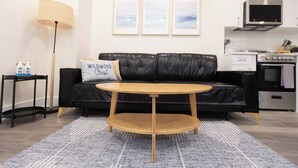 Ein modernes Wohnzimmer mit einer schwarzen Ledersofa, einem Holztisch, einer Lampe und gerahmten Kunstwerken an der Wand.