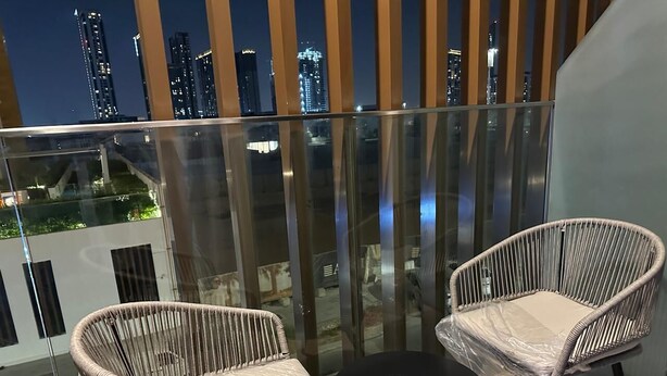A balcony with two wicker chairs and a small table, overlooking a cityscape at night. - VESTA - Luxury Studio - Riviera (I) (Dubai)