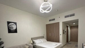 A modern bedroom with a bed, a sofa, a small round table, and a ceiling light fixture. - VESTA - Luxury Studio - Riviera (I) (Dubai)