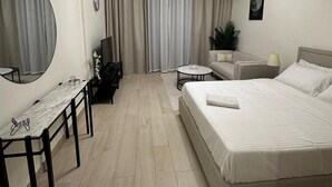 A modern hotel room with a bed, a desk, a chair, a round mirror, a round table, a sofa, a lamp, and a ceiling light fixture. - VESTA - Luxury Studio - Riviera (I) (Dubai)