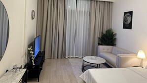 A hotel room with a bed, a sofa, a small round table, a TV, and curtains. - VESTA - Luxury Studio - Riviera (I) (Dubai)