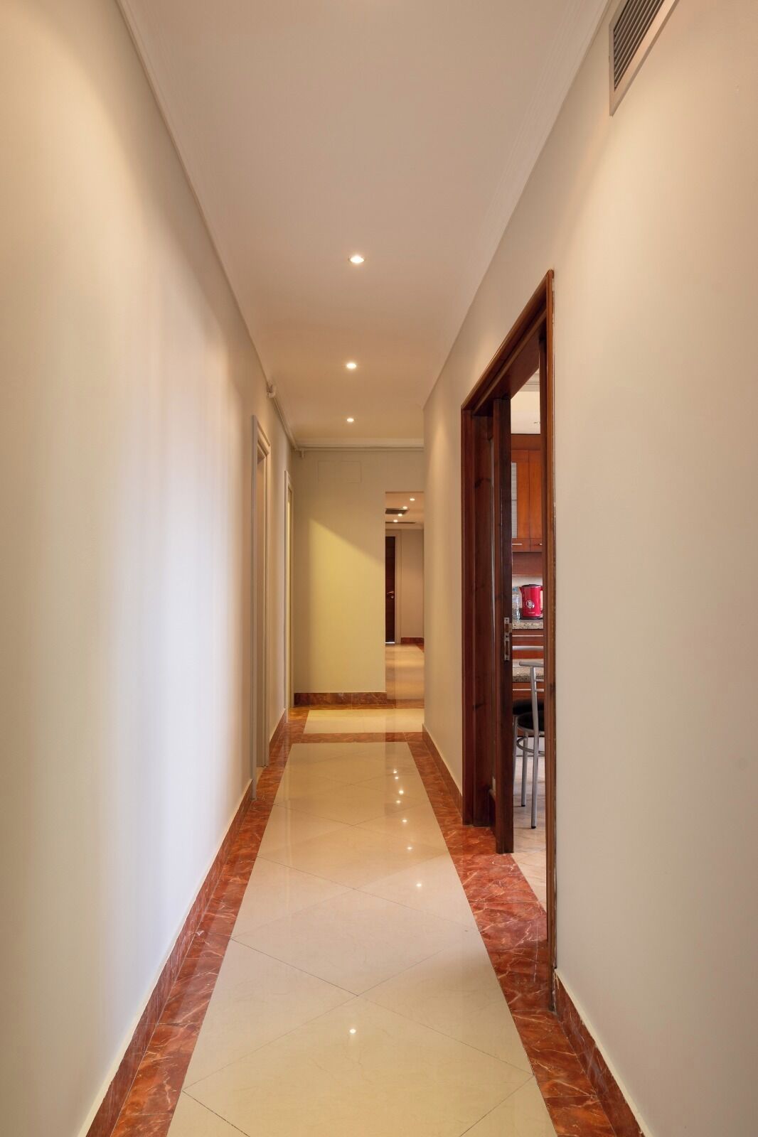 A hallway with a marble floor, white walls, and a wooden door leading to a room.